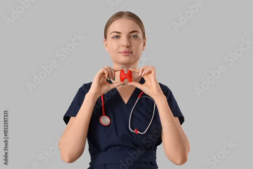 Female endocrinologist with thyroid gland model on grey background