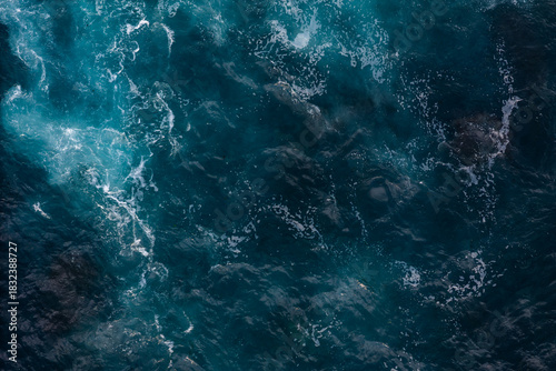 Ocean surface with white foam and dark lava reefs, aerial top down shot