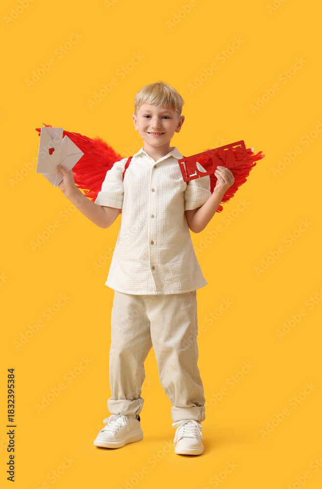 Obraz premium Cute little happy boy dressed as cupid with letters and word LOVE on yellow background. Valentine's Day celebration