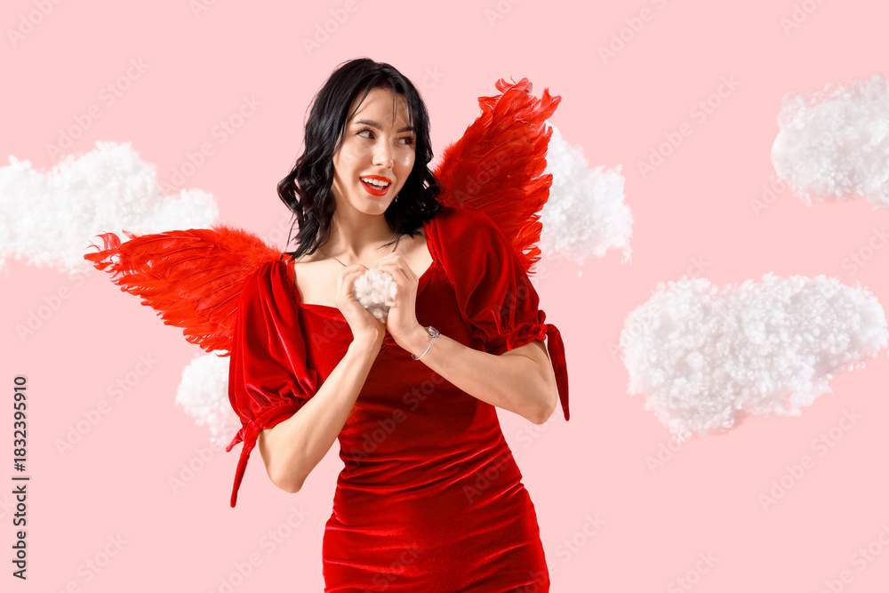 Obraz premium Beautiful young happy woman dressed as cupid in clouds showing heart gesture on pink background. Valentine's Day celebration