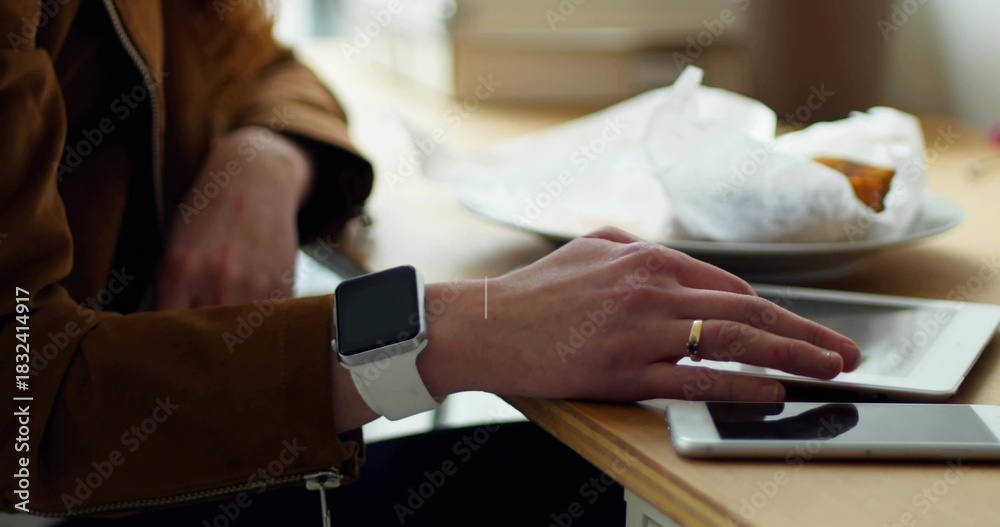 Obraz premium Touching white tablet with right hand wearing white smartwatch, gold ring at wood table near window
