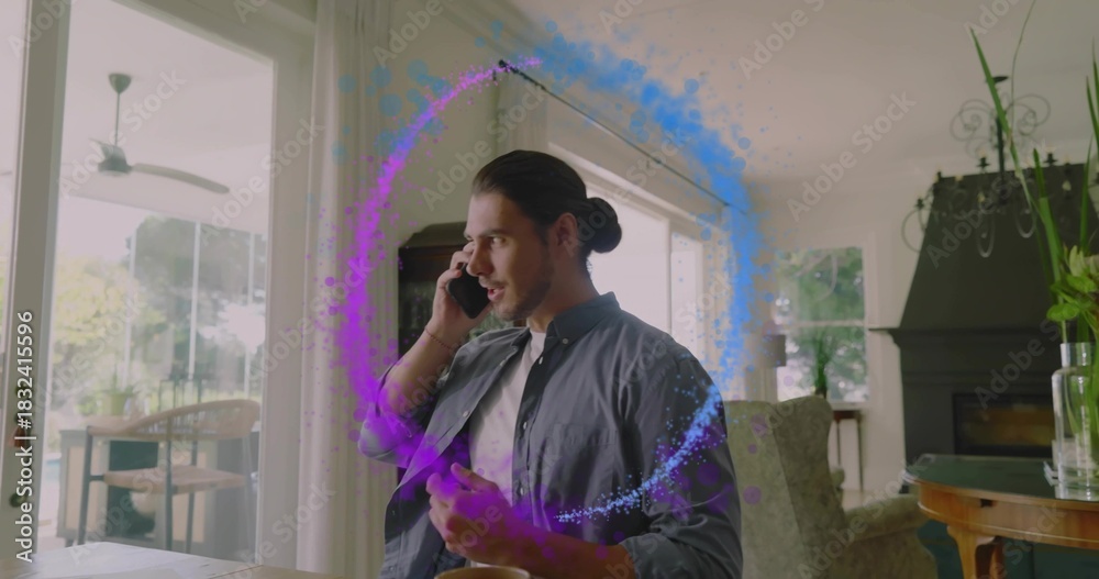 Naklejka premium Talking bun-haired man in dark shirt holding phone, gesturing at wooden table at home, purple ring