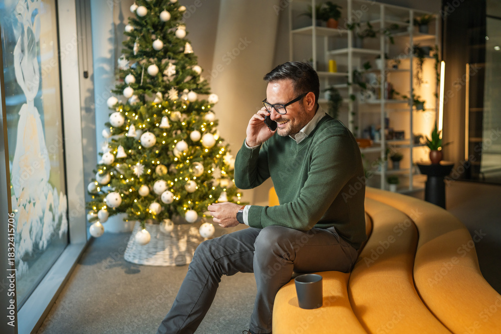 Obraz premium Man making phone call sitting by christmas tree in office