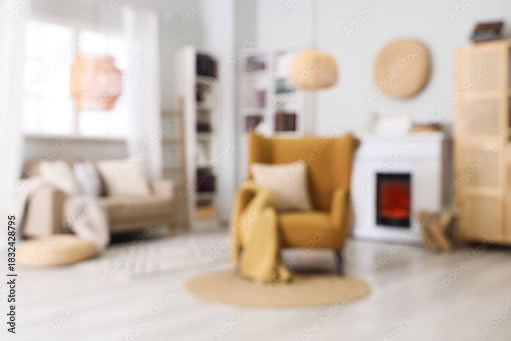 Fototapeta premium Blurred view of living room with comfortable armchair, sofa, fireplace and book shelves