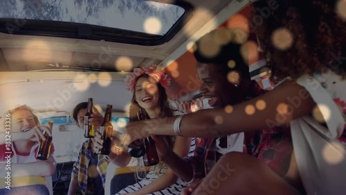 Friends raising bottles, clinking, cheering in retro van for events with gold bokeh softening faces