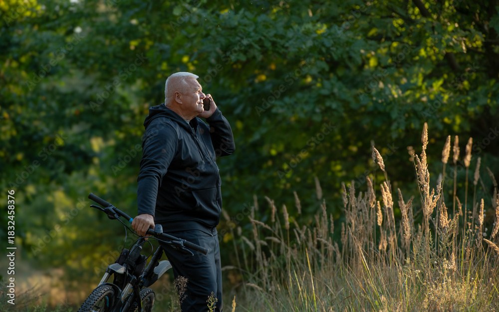 Fototapeta premium An elderly gray-haired man uses a smartphone while cycling through the forest.