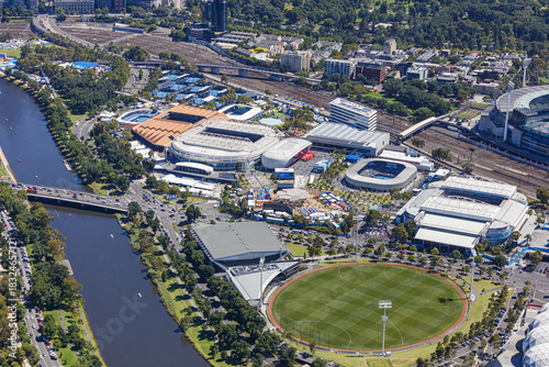 Aerial view of the Yarra River winding past the iconic Melbourne Park sporting complex, a vibrant tapestry of courts and stadiums under the summer sun, Melbourne, Victoria, Australia.