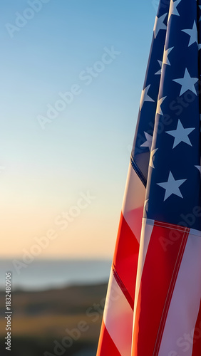 Vertical shot of the American flag with its bold red and white stripes against a serene and golden coastal sunset sky
