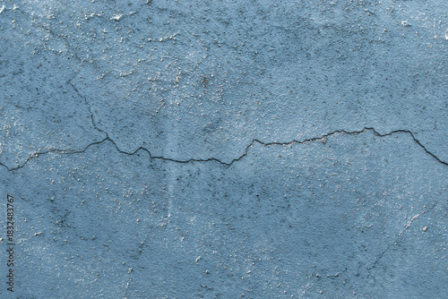 Texture of blue painted concrete wall with large horizontal crack showing deterioration and damage of old building construction structure