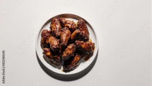 Delicious glazed chicken wings on a white plate, top view.