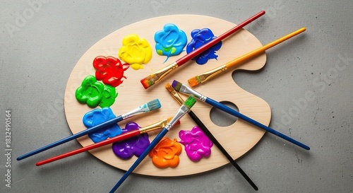 A wooden art palette with various paintbrushes and paint samples on a gray surface.