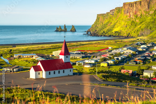 View of basalt stacks Reynisdrangar, black sand beach, church and city of Vik, Iceland