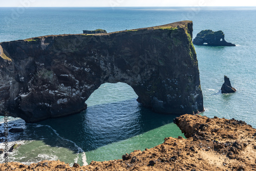 Dyrholaey coast cliffs and rocky arch, Vik, South Iceland. Reynisfjara ocean black volcanic sand beach in far.
