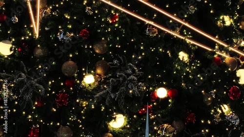 A glowing Christmas tree in the background, adorned with red and gold ornament balls, captures the festive spirit of the holiday season