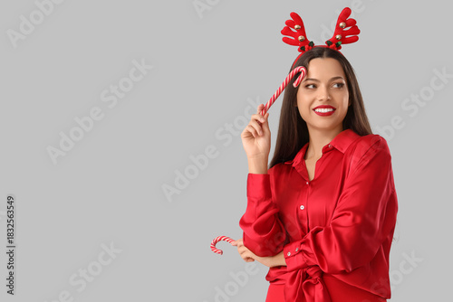 Happy young woman in red outfit and reindeer horns with candy canes on white ...