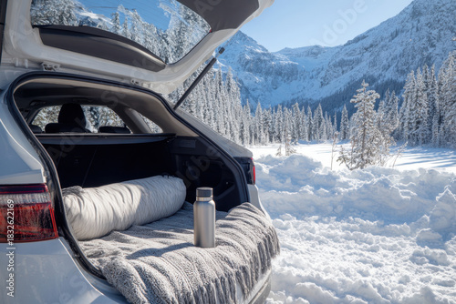 A car with an open trunk containing a thermos and a blanket in the winter mountains