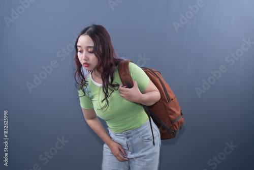 Asian woman in green dress wearing backpack looking down