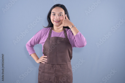 A woman in a brown apron is making a call me gesture with a smile