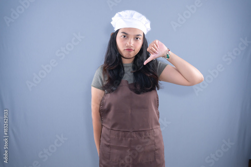 A woman in a chef's hat and brown apron gives a thumbs down