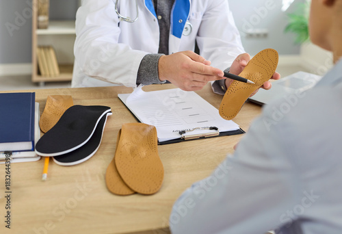 Orthopedist doctor shows orthopedic insoles to patient in medical clinic. They discuss custom orthotics and arch support to relieve foot pain. Concept medicine, foot healthcare and comfort.