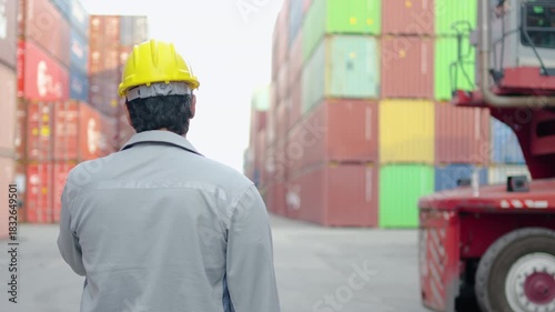 Back view of portrait engineer man talking radio with colleagues in container warehouse, checking for quality control, shipping export and import, then looking back at camera and smiling confidently