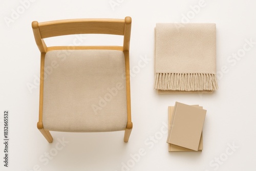 Top view wooden chair next to neatly folded beige throw blanket and small stack of hardcover books all arranged on bright white background