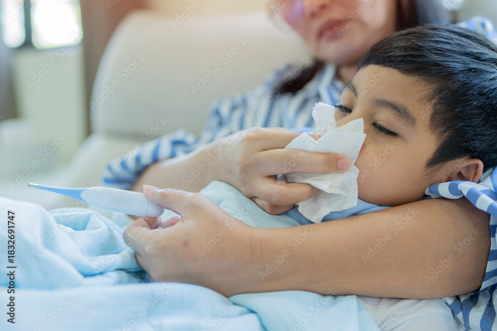 Obraz premium Sick child with high fever, mother holding thermometer and tissue for cleaning his nose