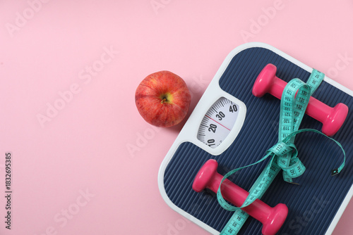 Scales, sneakers, dumbbells and measuring tape on a pink background
