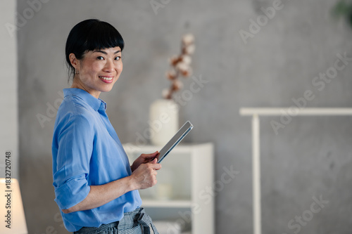 Asian hotel manager inspecting a room while holding a digital tablet, checking details and preparing the space in a modern hospitality setting