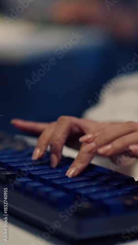 A vertical close-up of an Asian woman's hands typing rapidly on a modern illuminated computer keyboard while working alone late at night.