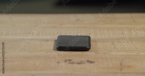 Resting folded black electronic device sitting centered on light wooden tabletop, showing scratches
