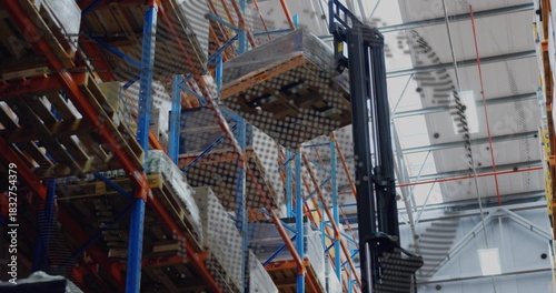 Lifting forklift mast holding wrapped pallet in large warehouse, showing pallet racking