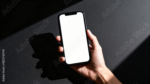 Hand holding smartphone with blank white screen on dark background, modern mobile device mockup for app or UI design  
