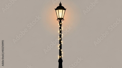 A classic black lamppost adorned with a string of warm glowing fairy lights against a soft muted background