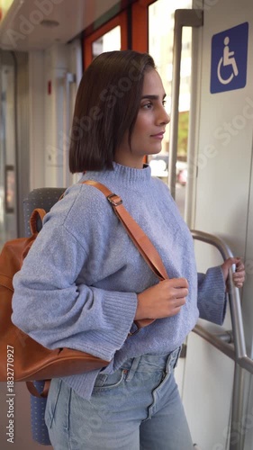 Young woman with a backpack standing inside a moving train and looking out the window