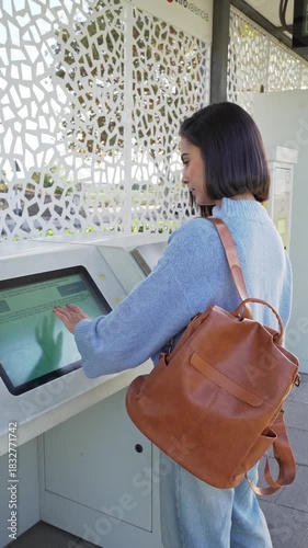 Young commuter woman with backpack buying metro ticket at an outdoor automated kiosk