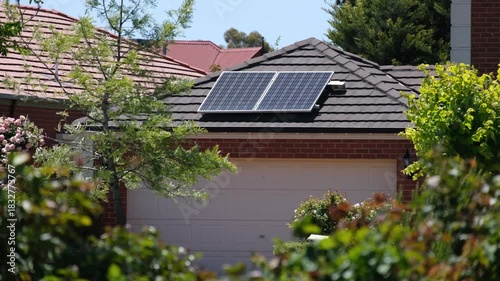 A suburban house in Australia featuring rooftop solar panels installed on a tiled garage roof. Concept of residential renewable energy, sustainable living, eco-friendly home upgrades, modern housing
