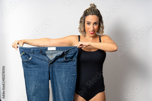 Woman showing significant weight loss success with old jeans