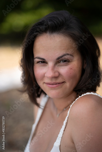 Vertical chest-up portrait of smiling dark-haired woman in swimsuit looking at camera, summer beach lifestyle with copy space and blurred background