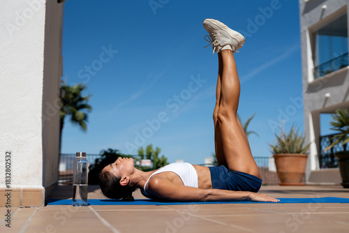 Foto Athletic woman in sportswear performing leg raise exercise on yoga mat outdoors,