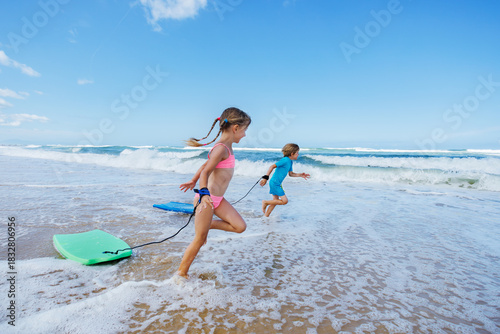 Children joyfully play and run by the ocean with boogie boards