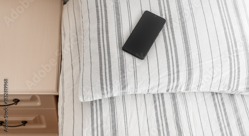 Smartphone on a striped pillow next to a bedside table