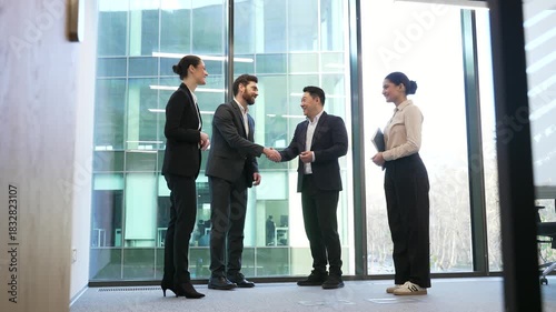 Meeting of group business people shaking hands in lobby of modern business center. Professional diverse men and women exchanging partner handshake standing in glass office. Collaboration and teamwork