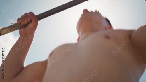 physically fit man performs pullup outside, athletic individual lifts himself at bright daylight outdoors, fitness enthusiast engages in outdoor strength training under clear sunny sky