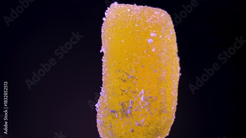 Single Yellow Marmalade Candy rotating on black. Macro studio shot of Lemon or Pineapple gummy sweet coated with sugar. Concept of Vitamin C or sugary dessert.