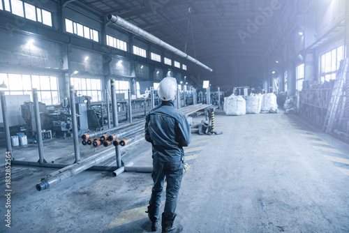 man working at a steel mill with a crane lifting steel pipes in blue tones
