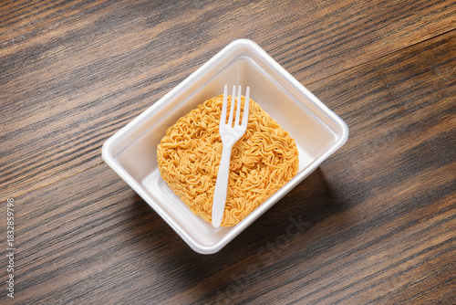 Dried instant noodles and white disposable fork in plastic plate