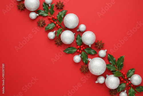 Christmas diagonal composition with white baubles, holly berries, and star anise on a bright red background. Festive flat lay for holiday or winter design.