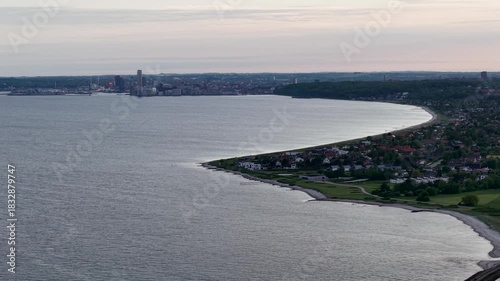 Wallpaper Mural Aerial panorama of a calm bay at sunset with a curving shoreline, adjoining village and distant city skyline under pastel evening skies. Torontodigital.ca