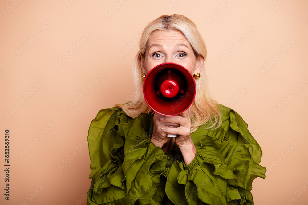 Obraz premium Mature woman with red megaphone speaks for advertising promotion in casual glamorous style against beige background